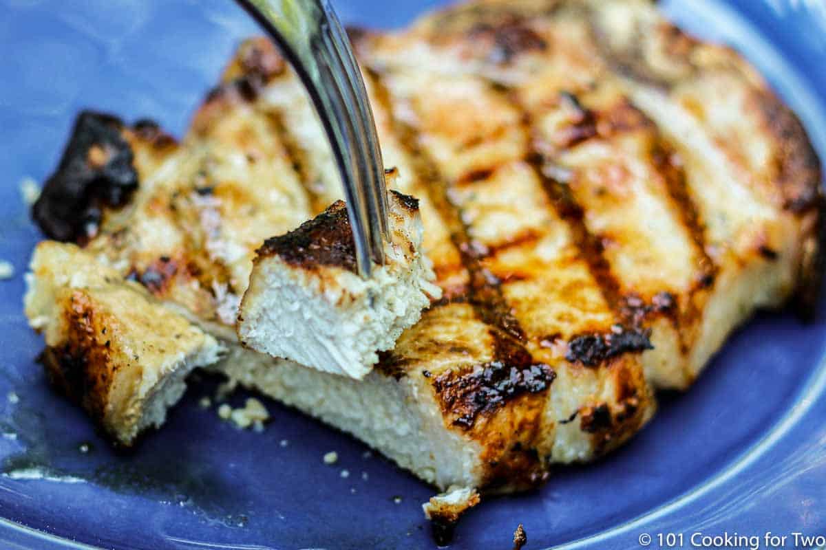 Bite of pork chop on fork over blue plate