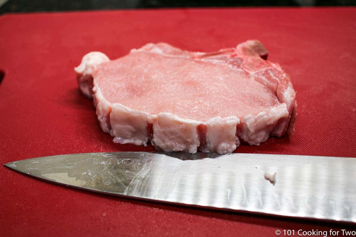 trimmed pork chop on red board.