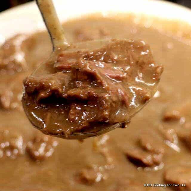 close up image of beef and gravy in a large spoon over a full serving dish
