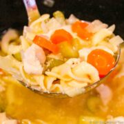 Ladle of chicken noodle soup over the crock pot