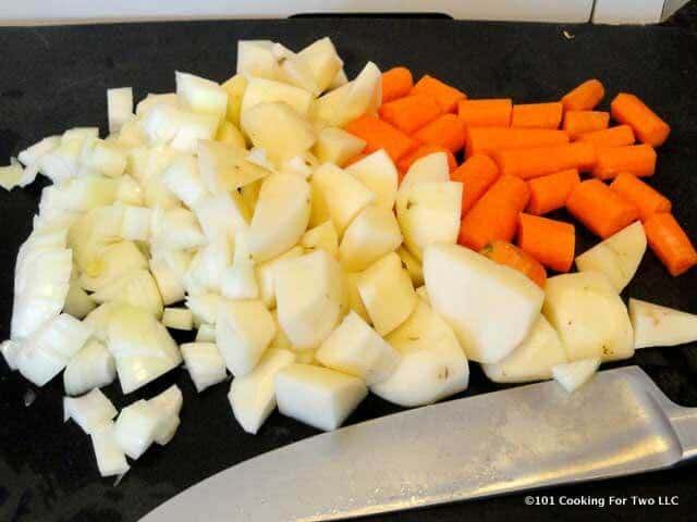 a pile of chopped up potatoes and carrots on a black chopping board