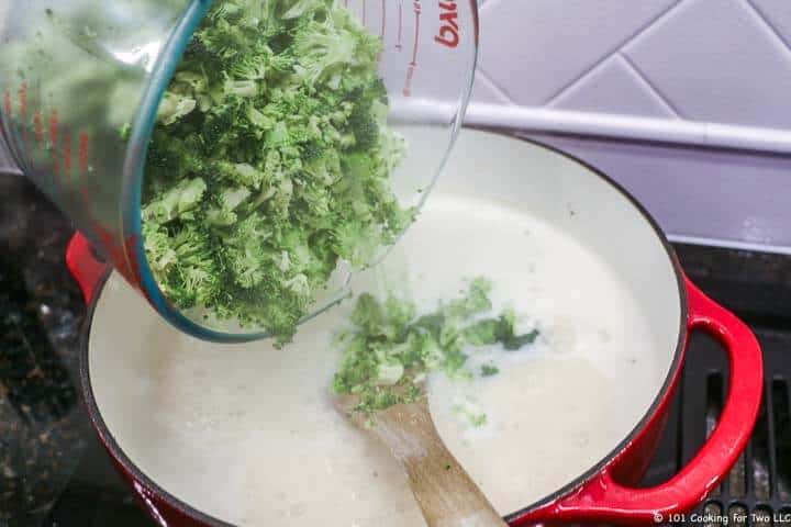adding chopped broccoli to soup pan