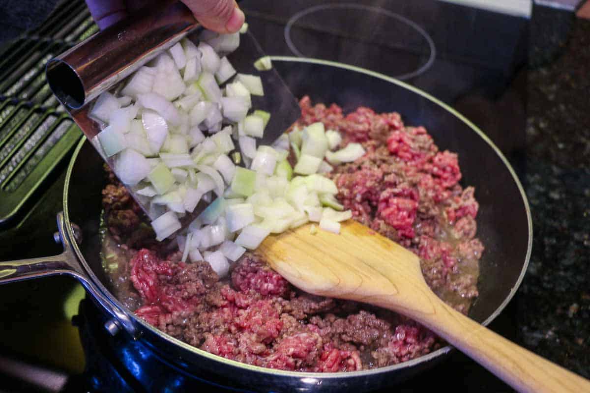 adding chopped onion to burger in pan