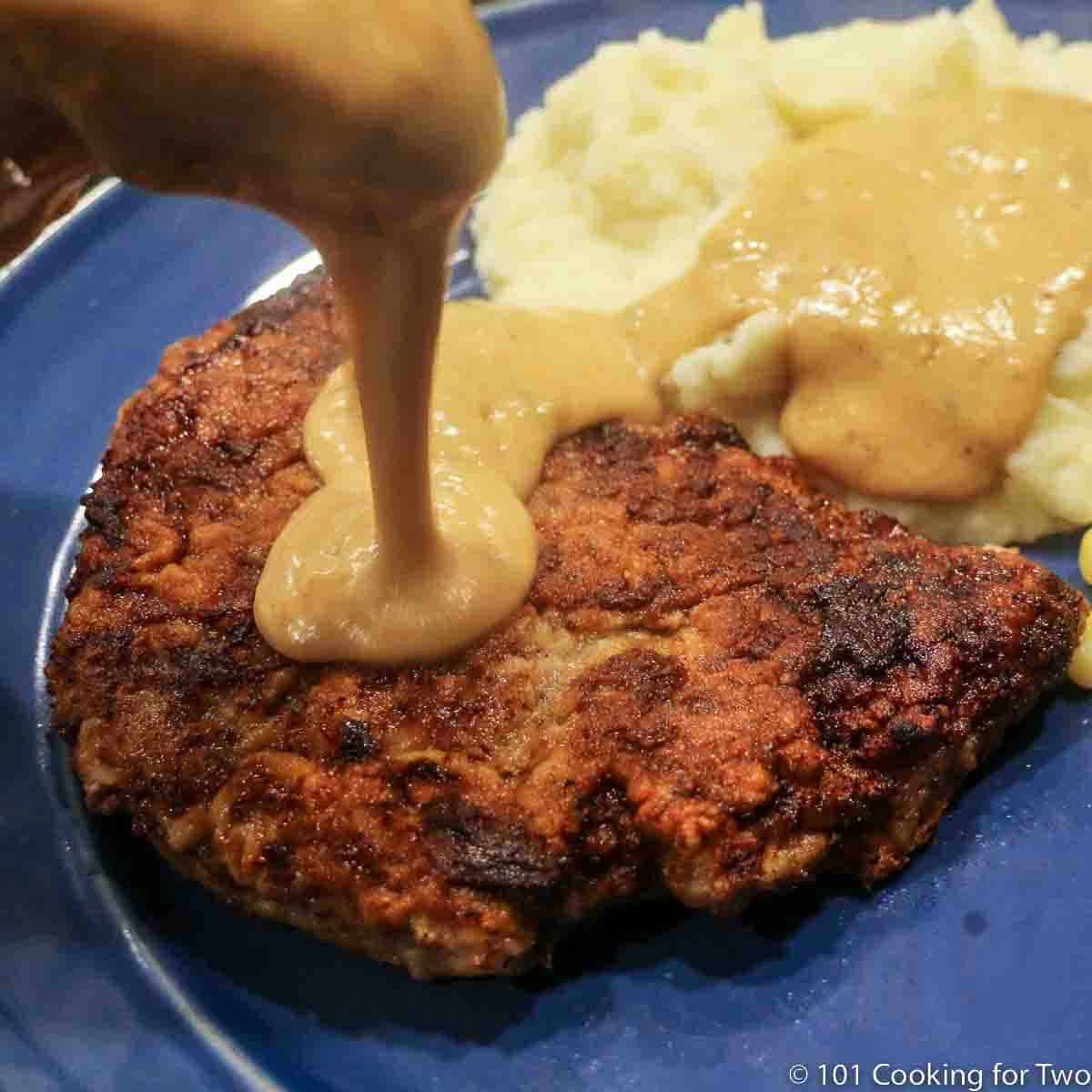image of chicken fried steak on a blue plate with potatoes being covered with gravy