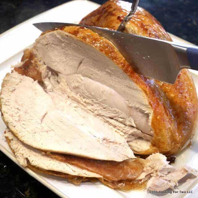 turkey breast being carved with large fork and knive on white platter