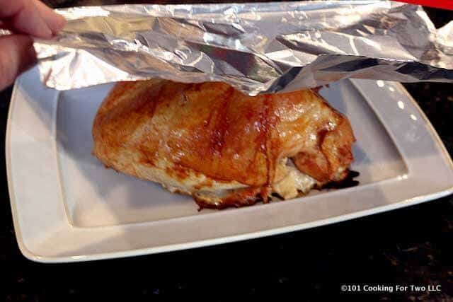 image of the cooked turkey breast on a white platter being tented with foil