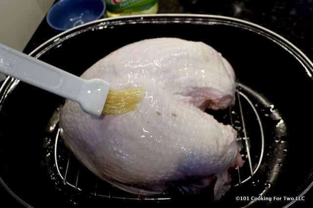 a picture of the turkey breast in a roasting pan being brushed with oil