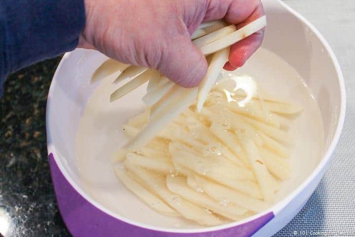 adding fries to water to soak in bowl