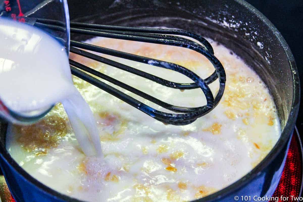 adding milk to saucepan with whisk