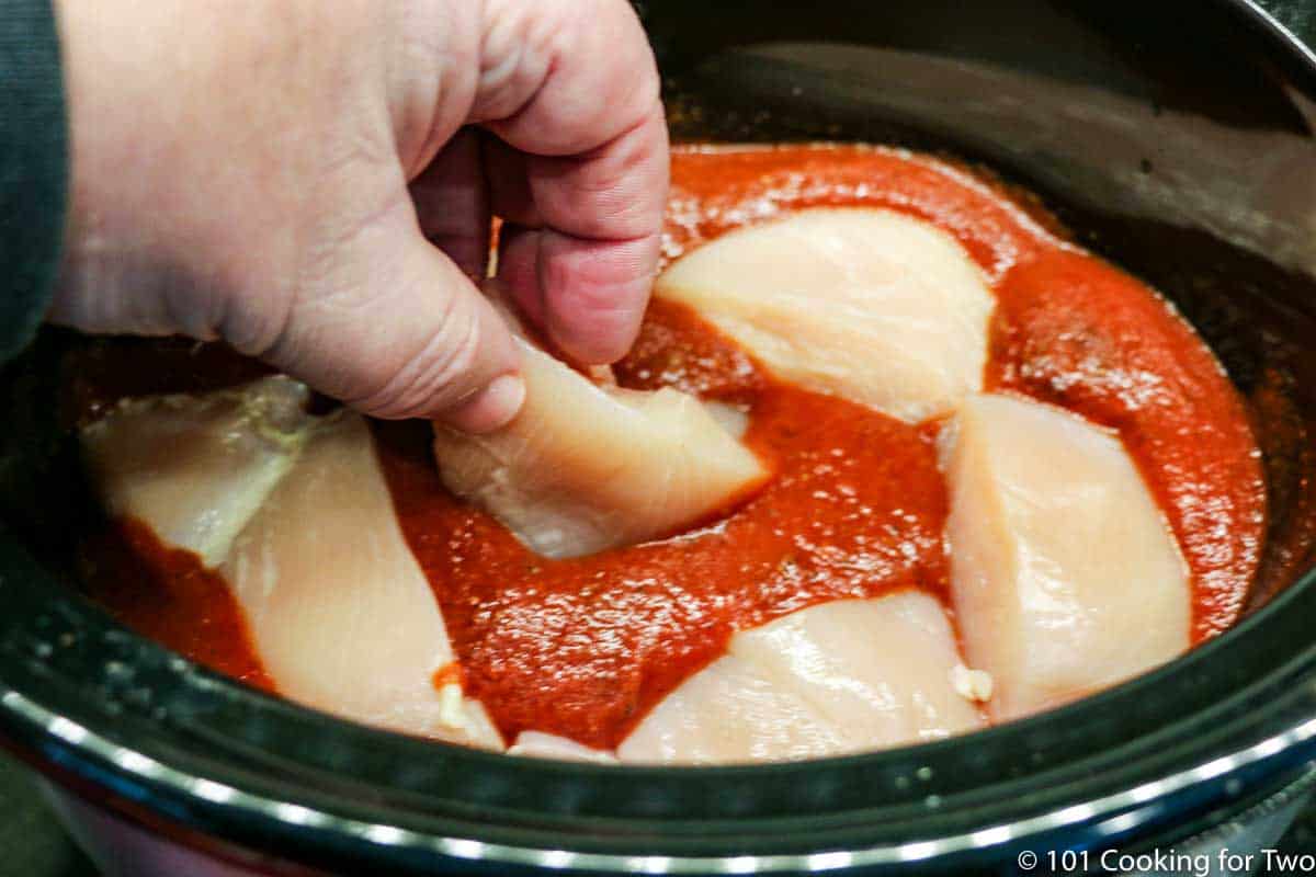 adding raw chicken pieces to sauce in crock pot