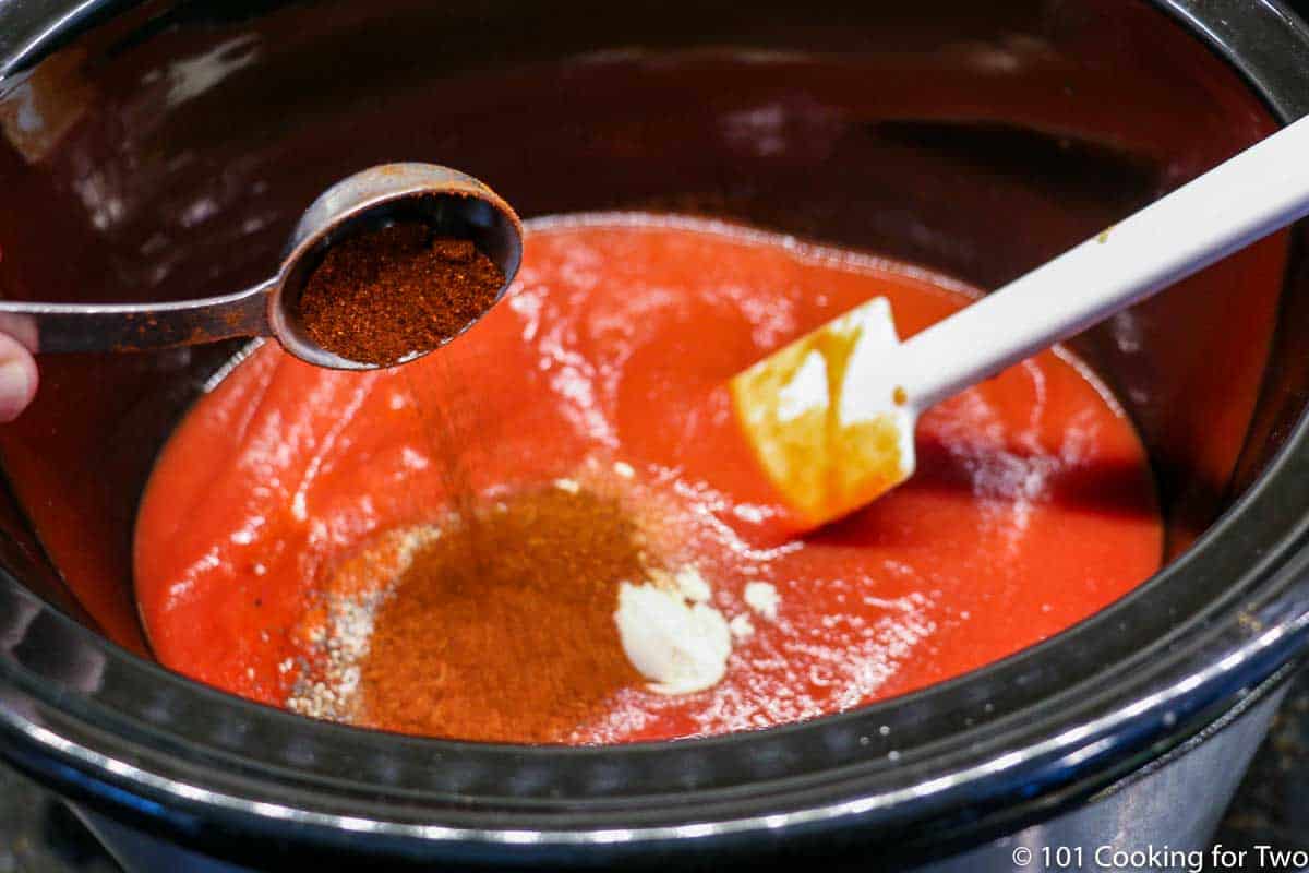 adding spices to crock pot with sauce