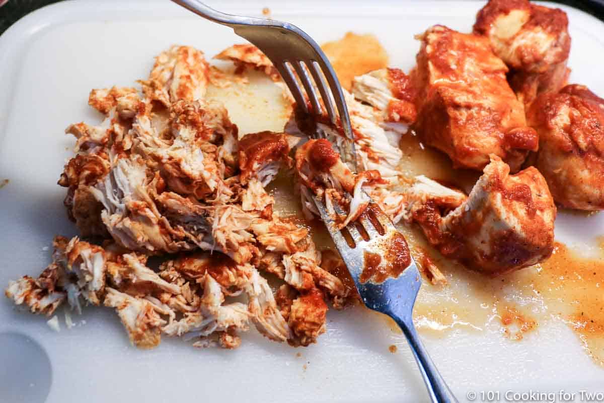 shredding chicken on white board with forks