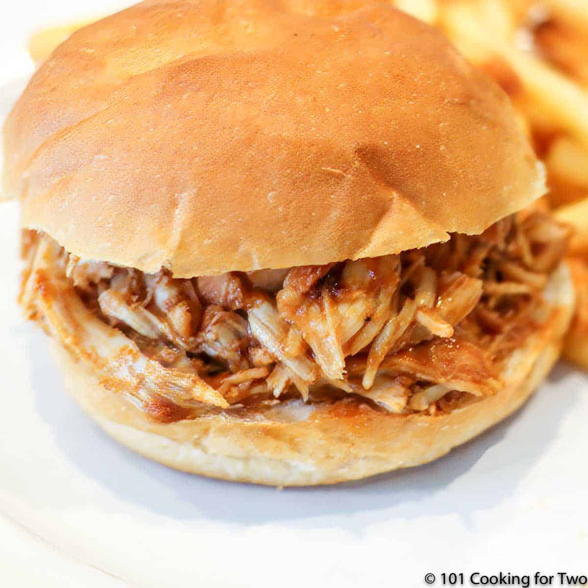 close up picture of a bbq chicken sandwich on a bun on a white plate