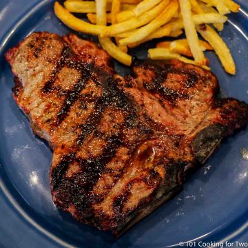 Picture of a nice porterhouse steak with grill marks on a blue plate with french fries