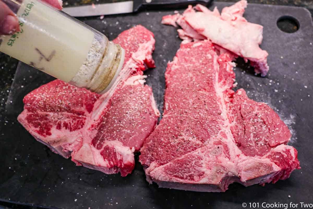 porterhouse steaks trimmed of fat being seasond on black board.