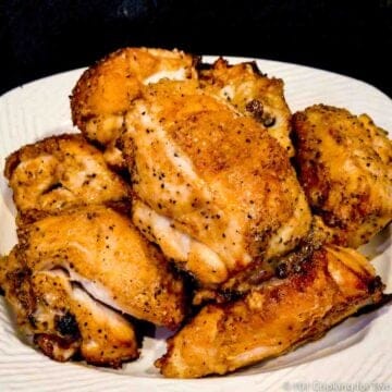 Pile of split (bone-in) chicken breasts on white plate