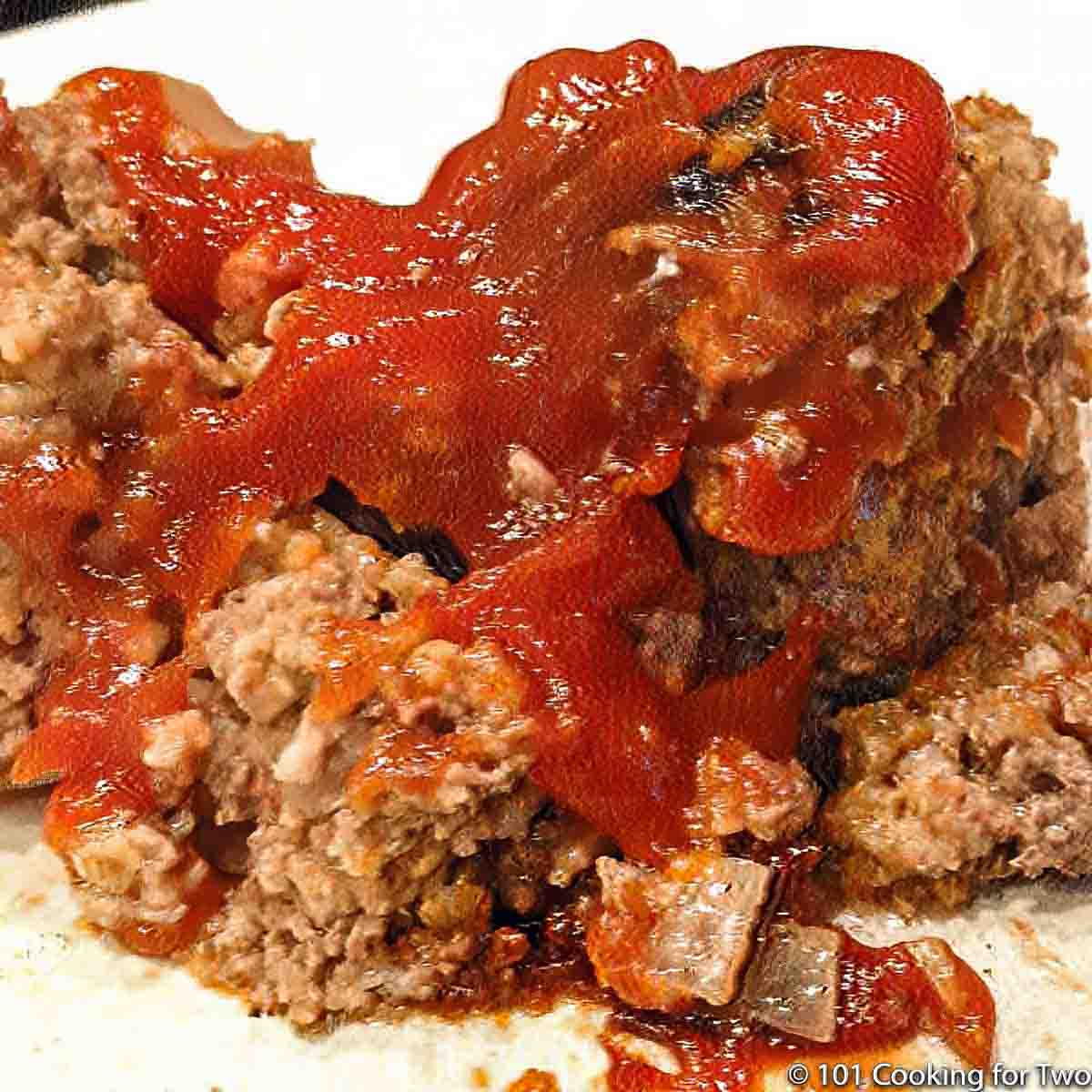 close up image of a large serving of meatloaf with ketchup on a white plate