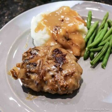 Salisbury Steak on a gray plate with potatoes and gravy.