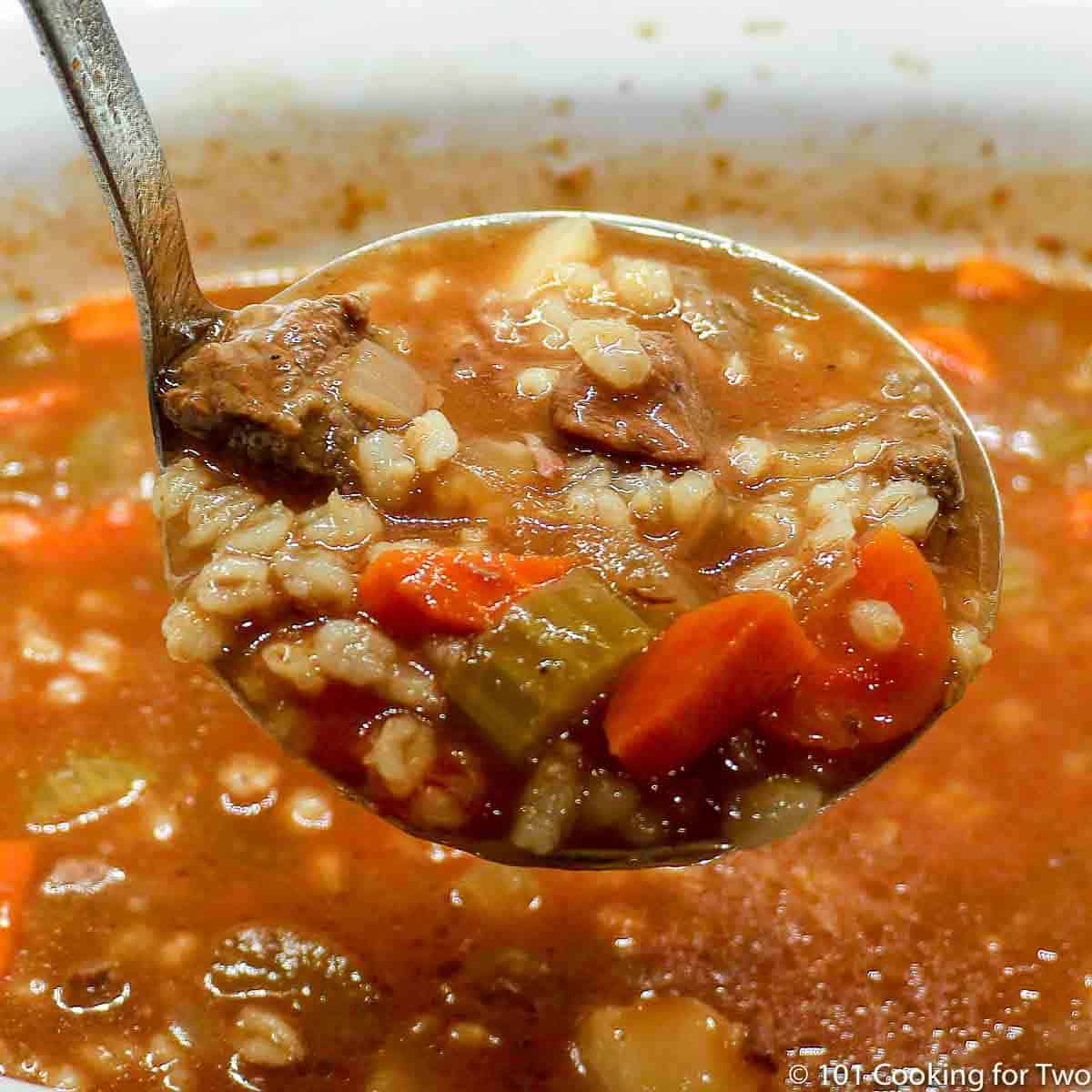 A ladle of beef barley soup over a full crock pot.