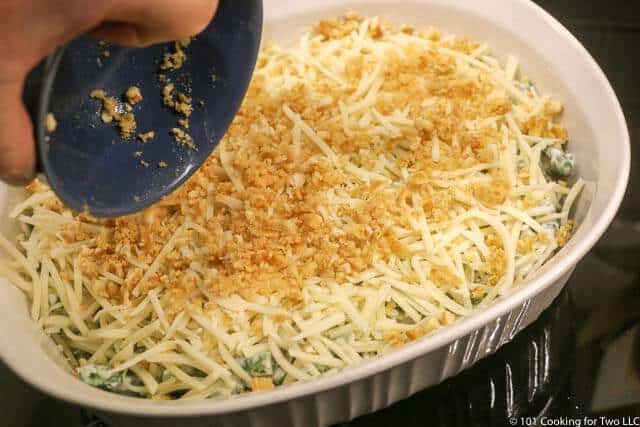 image of adding the topping to the casserole that is already covered with cheese in a white baking dish