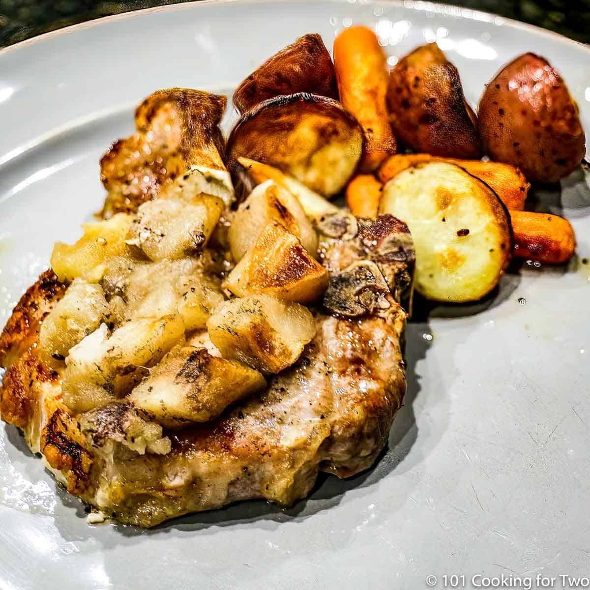 apple pork chops on a gray plate with carrots and potatoes.