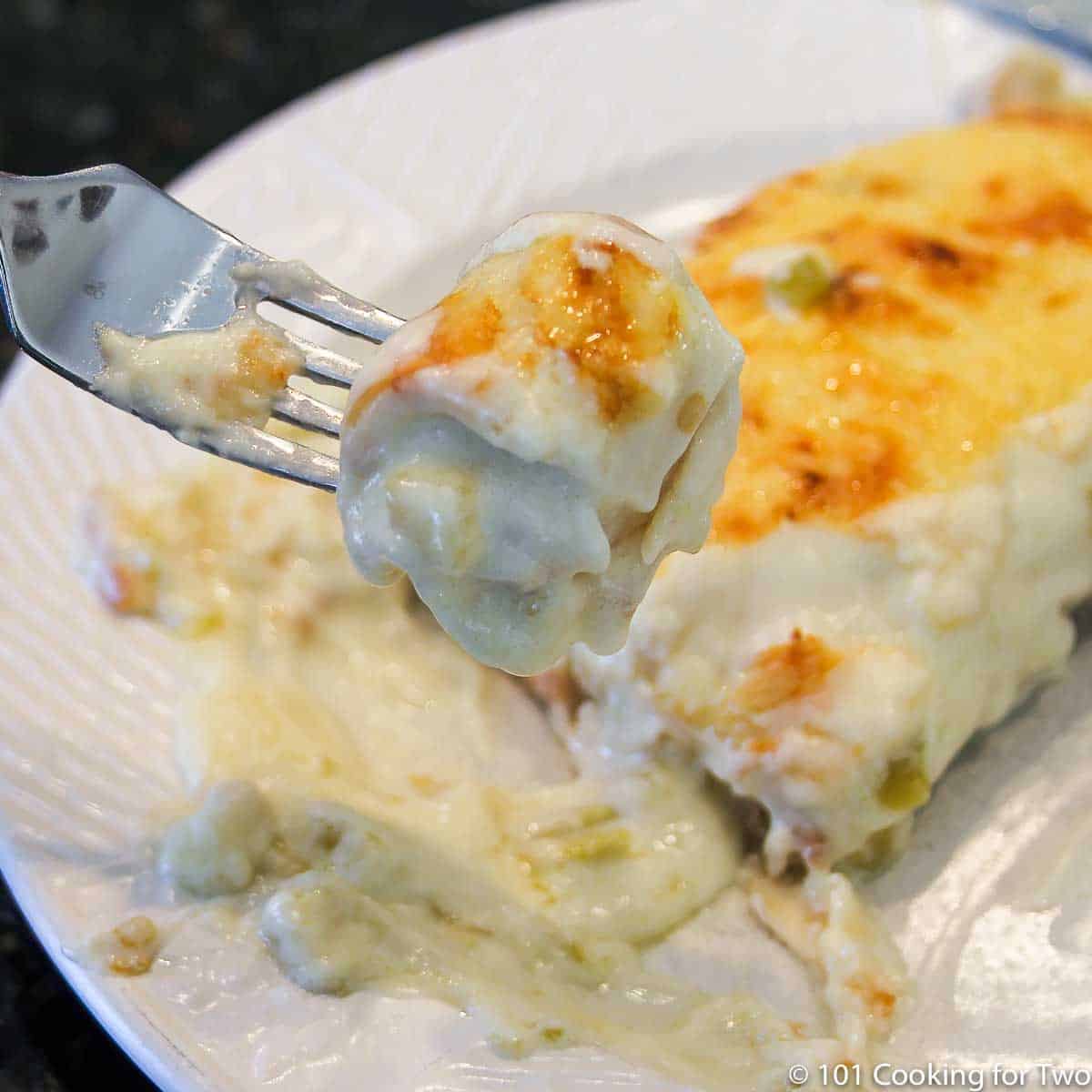 Close up image of a bite of enchilada over a white plate with an enchilada.