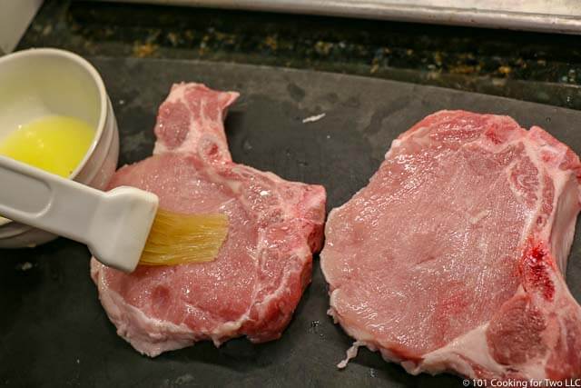 image of two pork chops on a black cutting board being brushed with melted butter