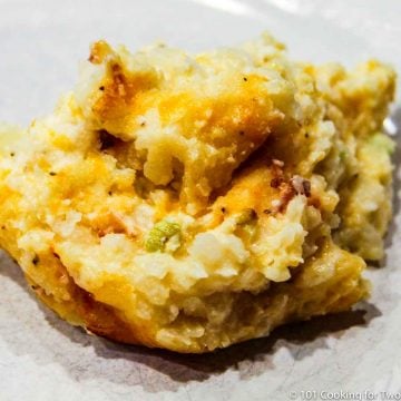 close up image of cheesy potato casserole on a white plate