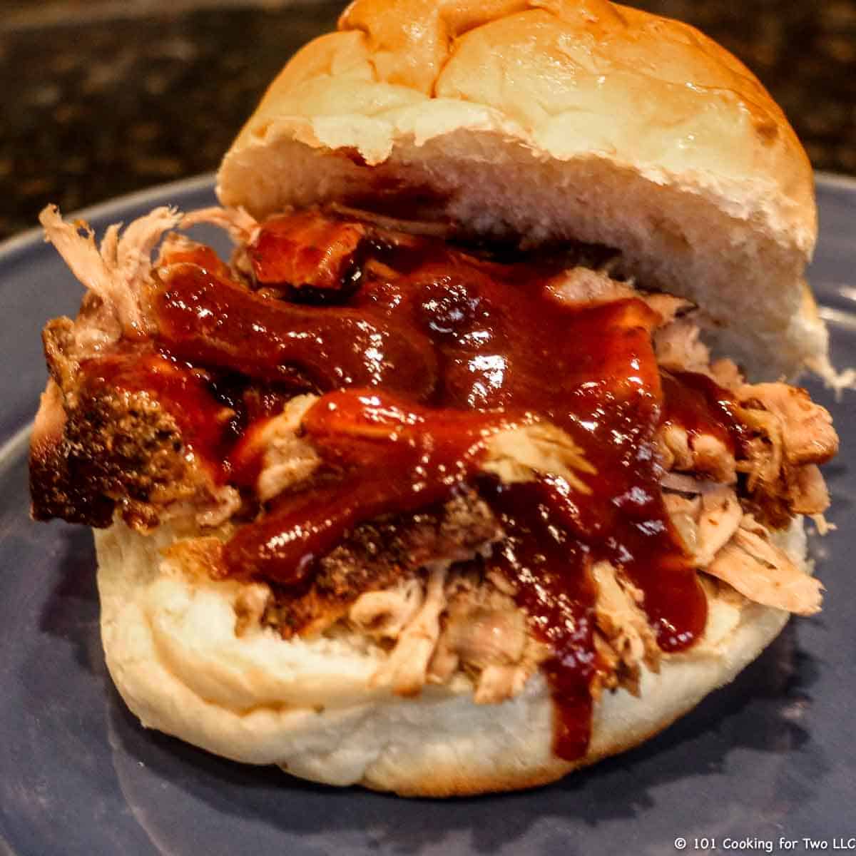 BBQ pulled pork sandwich with sauce on a blue plate.