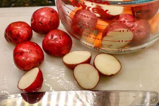 image of smaller red potatoes being cut in half on a white cutting board