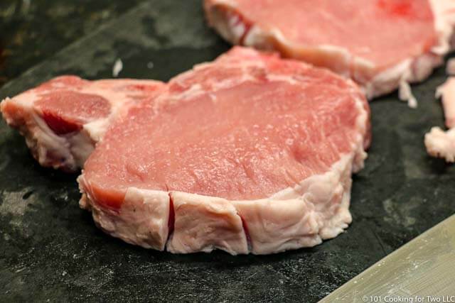 image of a pork chop on a black cutting board with the fat cut