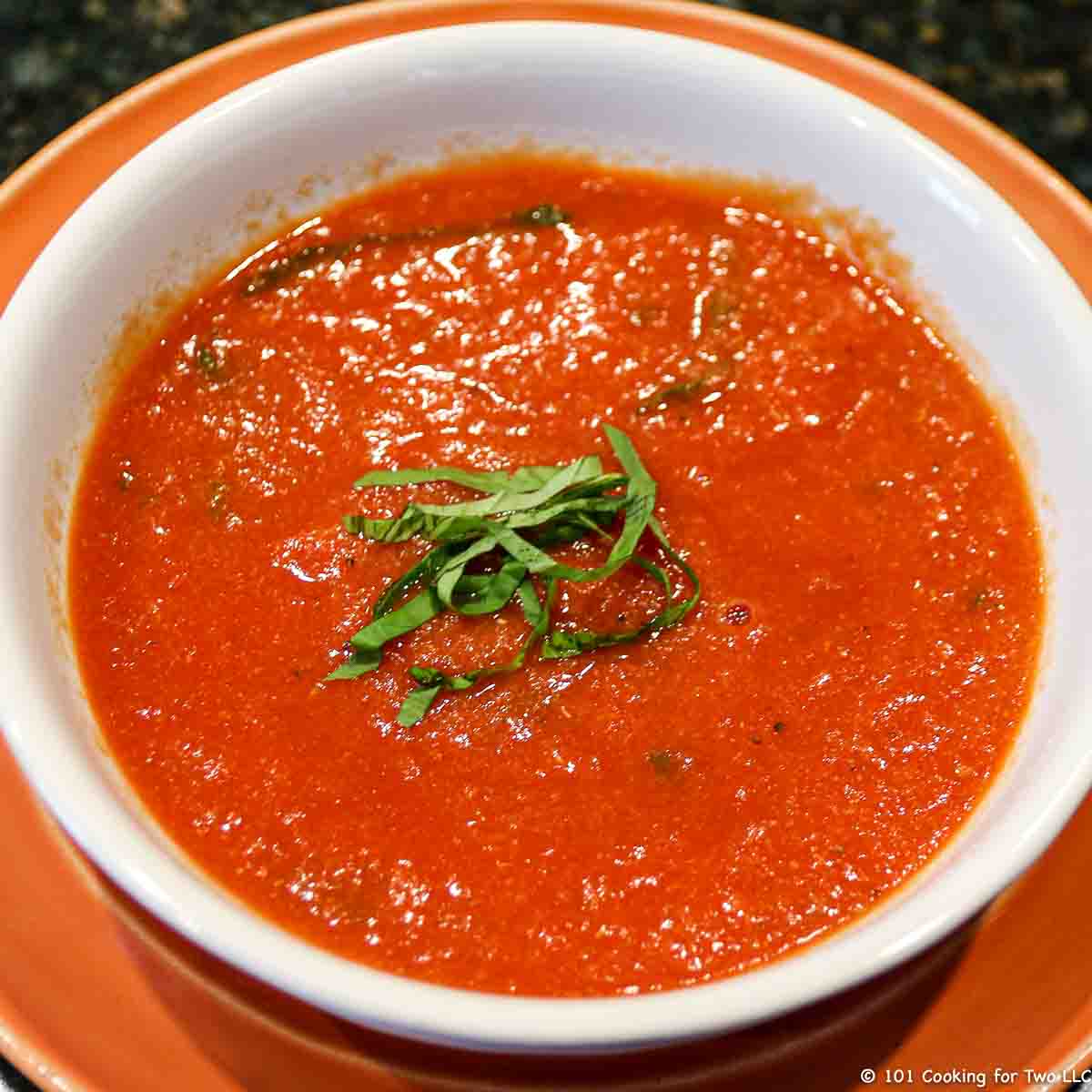 image of a bowl of tomato basil soup in a white bowl on orange plate