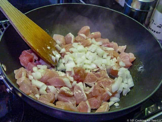 image of cooking chicken and onion in black pan