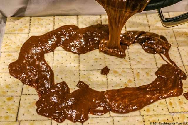 Pouring carmel over the crackers on a tray.