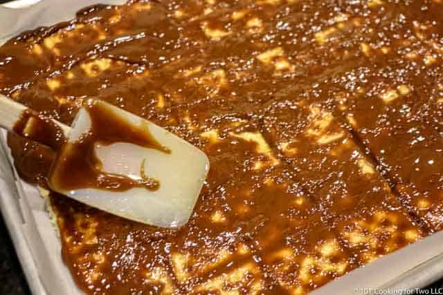 Spreading the toffee over the crackers with a spatula.