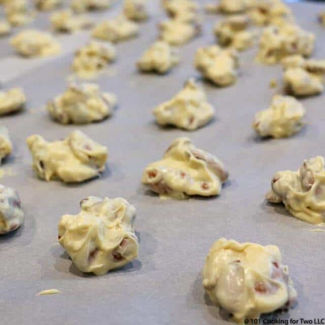 image of lots of white chocolate almond clusters cooling on parchment paper.