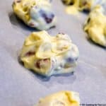 A closeup image of a white chocolate almond cluster on white parchment paper