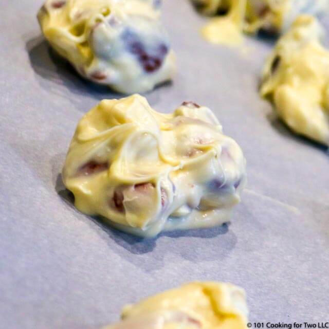 A closeup image of a white chocolate almond cluster on white parchment paper