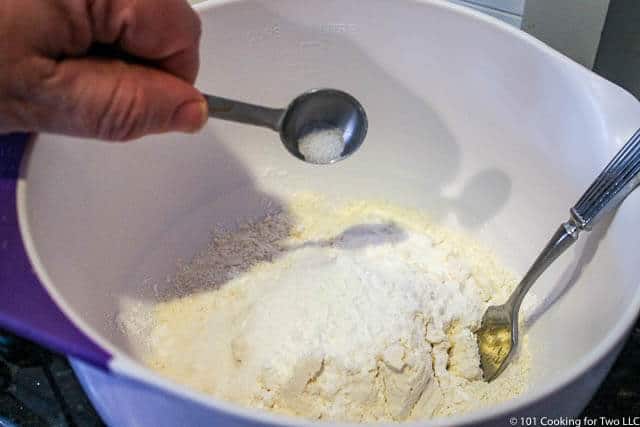 adding ingredients for biscuits to a white bowl
