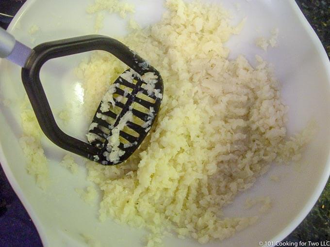 image of mashing cauliflower in a white bowl.