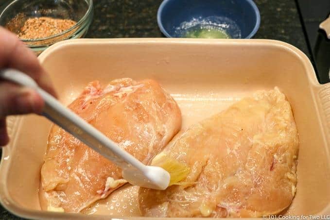 brushing the chicken in the dish with butter