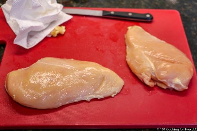 image of raw chicken breast trimmed on red board