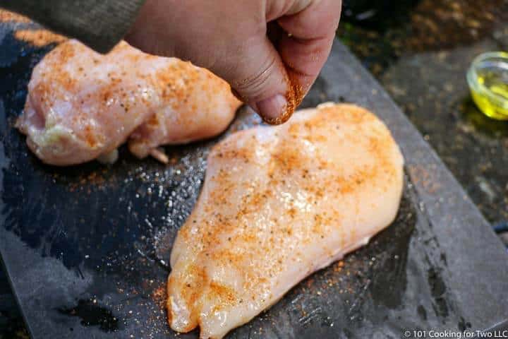 sprinkling spices on raw chicken breasts
