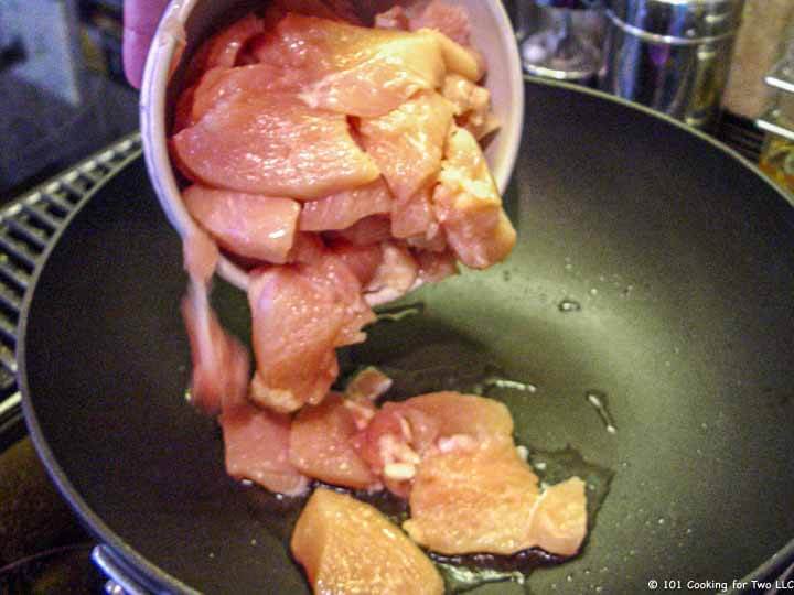 adding raw chicken to fry pan
