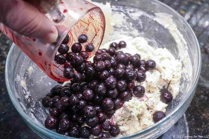 pouring blueberries into bowl with dough.