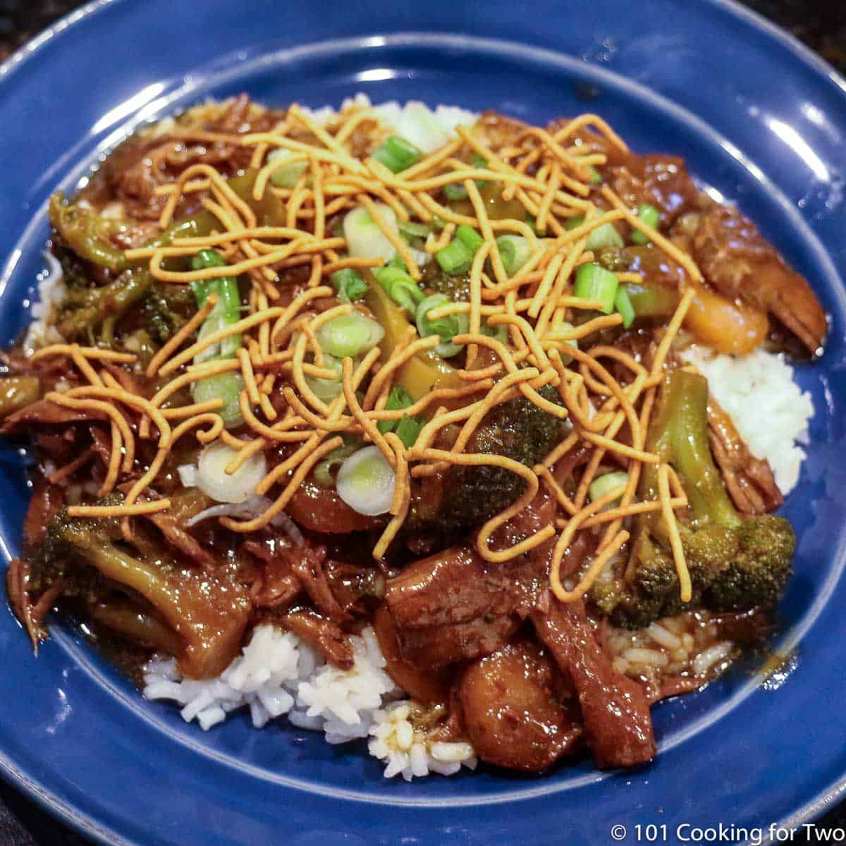 beef and broccoli with rice and toppings on blue plate.