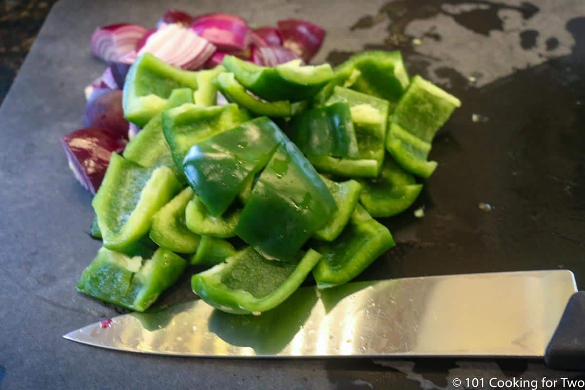 cut up pepper and red onion on black board,