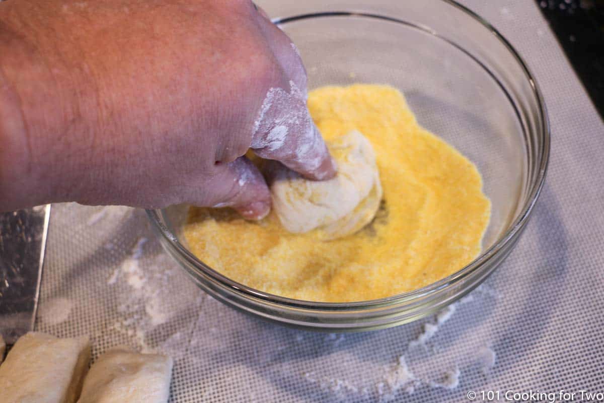 dipping raw dough into bowl of corn meal