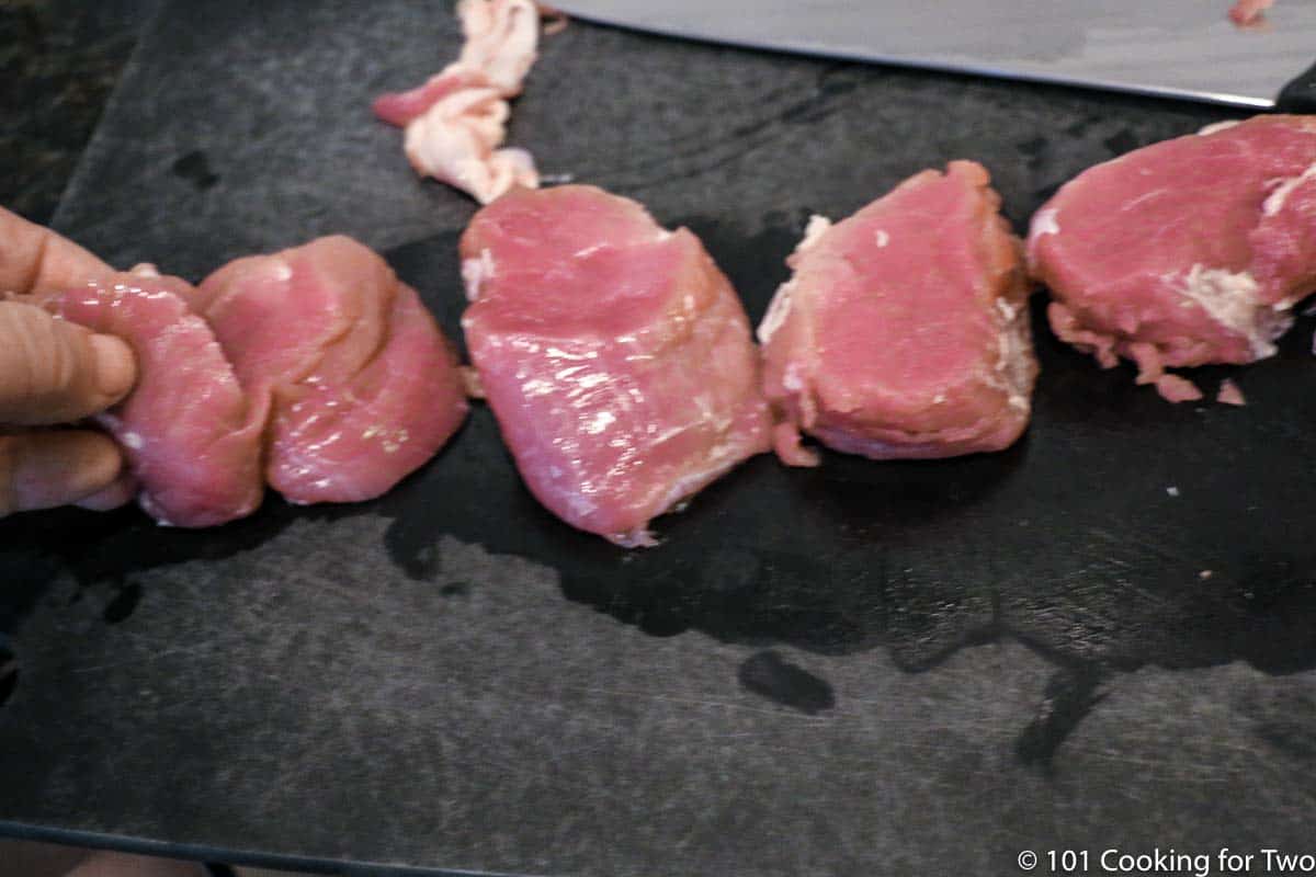 slices of pork tenderloin on black board.