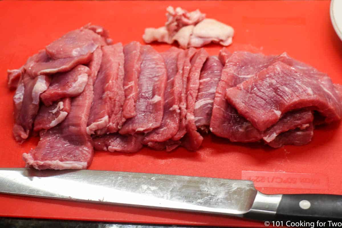 thinly sliced beef on red board.